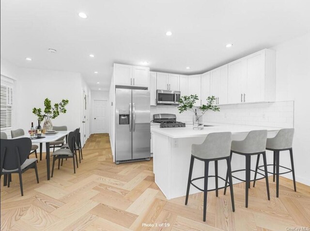 kitchen featuring a breakfast bar, white cabinets, kitchen peninsula, stainless steel appliances, and light parquet flooring