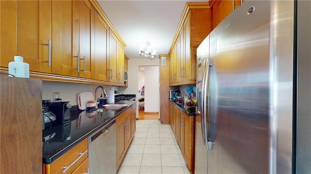 kitchen featuring stainless steel appliances, sink, light tile patterned floors, a notable chandelier, and dark stone countertops