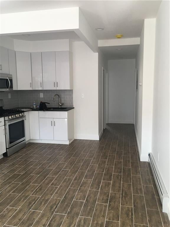 kitchen featuring baseboard heating, stainless steel appliances, white cabinets, sink, and backsplash