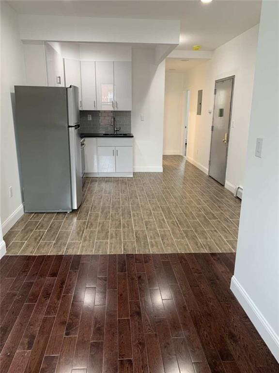 kitchen with decorative backsplash, white cabinets, light wood-type flooring, sink, and stainless steel refrigerator