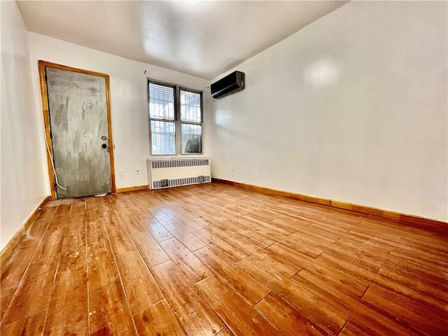 unfurnished room with a wall unit AC, radiator heating unit, and light hardwood / wood-style floors