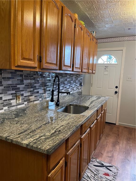 kitchen with wood-type flooring, stone countertops, tasteful backsplash, and sink