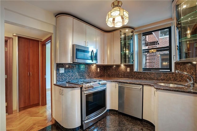 kitchen with appliances with stainless steel finishes, tasteful backsplash, sink, dark stone counters, and light parquet floors