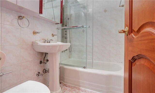 bathroom featuring combined bath / shower with glass door, tile walls, and toilet