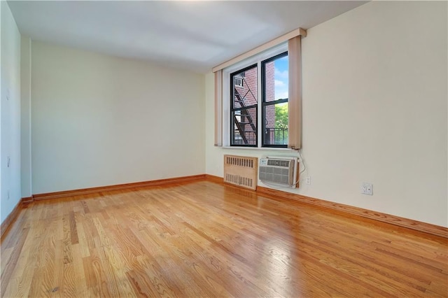 unfurnished room featuring radiator, a wall unit AC, and light wood-type flooring