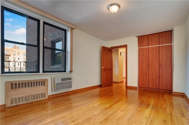 unfurnished bedroom featuring radiator heating unit, light wood-type flooring, a closet, and an AC wall unit