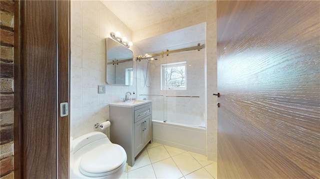 full bathroom with tile walls, tile patterned flooring, bath / shower combo with glass door, vanity, and toilet