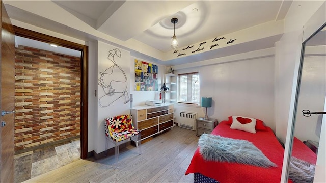 bedroom with hardwood / wood-style floors, brick wall, and radiator heating unit