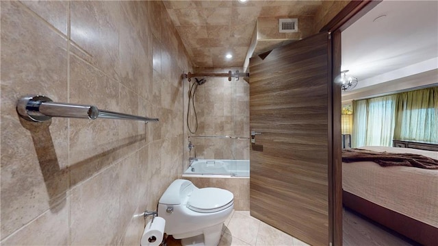 bathroom featuring tile patterned floors, toilet, shower / bath combination, and tile walls