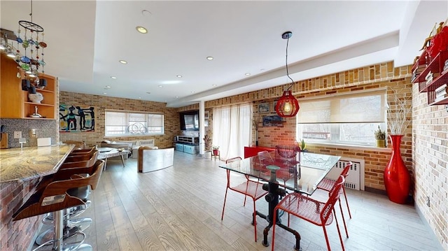 dining area with light wood-type flooring, radiator heating unit, and brick wall