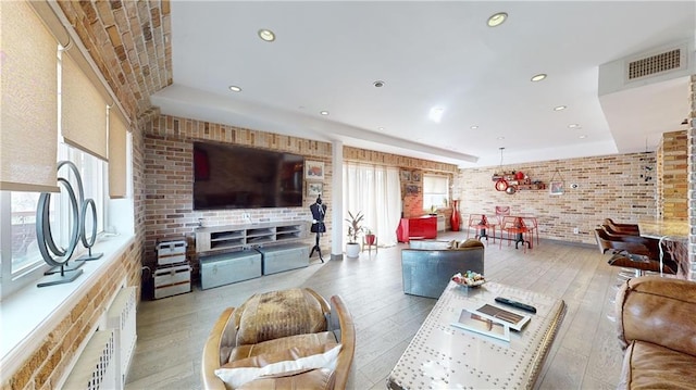 living room with brick wall, light hardwood / wood-style floors, and plenty of natural light