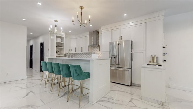 kitchen featuring a chandelier, stainless steel fridge with ice dispenser, white cabinetry, wall chimney range hood, and decorative light fixtures