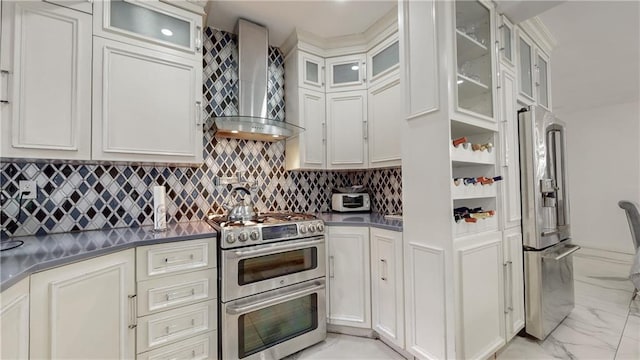 kitchen featuring decorative backsplash, wall chimney range hood, stainless steel appliances, and white cabinets