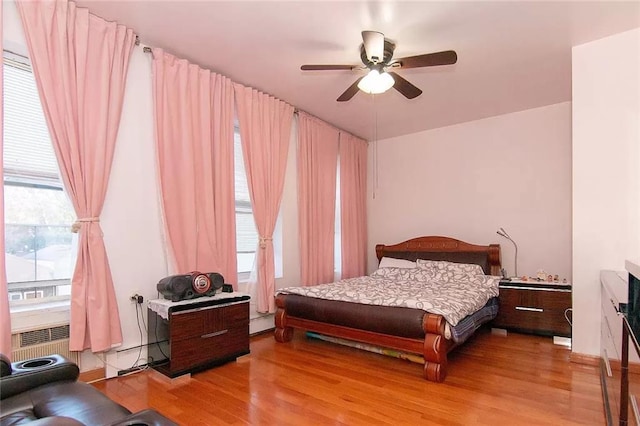 bedroom featuring a baseboard heating unit, ceiling fan, and wood finished floors