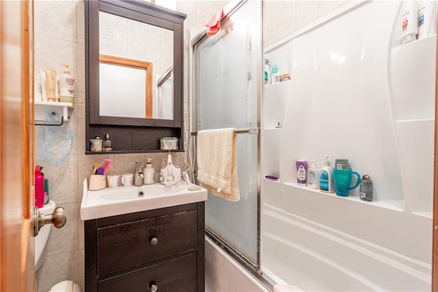 bathroom featuring toilet, enclosed tub / shower combo, backsplash, vanity, and tile walls