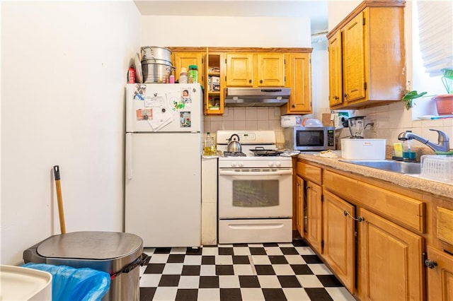 kitchen with white appliances, dark floors, light countertops, under cabinet range hood, and a sink