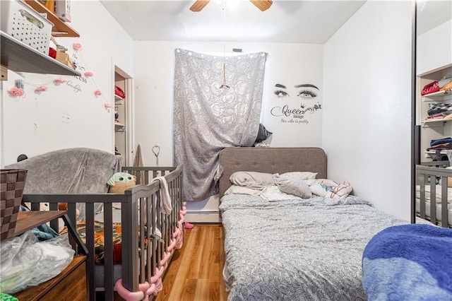 bedroom with ceiling fan, baseboard heating, and wood finished floors