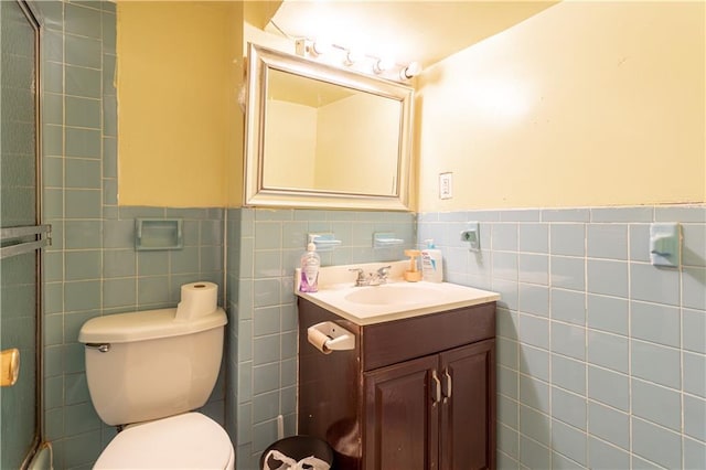 bathroom with a shower with shower door, vanity, toilet, and tile walls