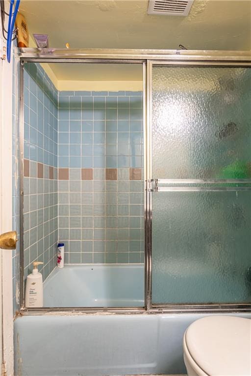 bathroom featuring toilet, enclosed tub / shower combo, and visible vents