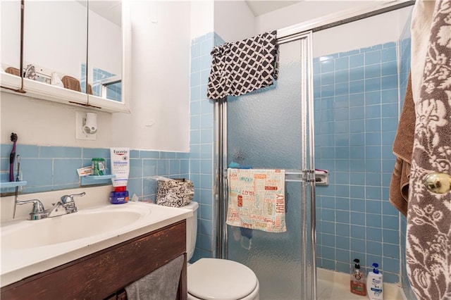 bathroom with toilet, a shower stall, tile walls, and vanity