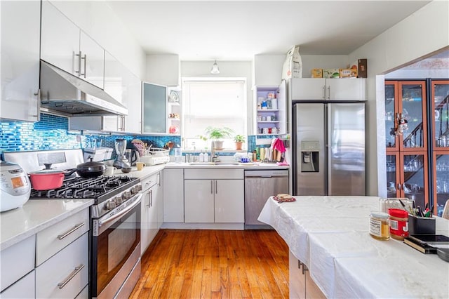 kitchen featuring appliances with stainless steel finishes, light countertops, under cabinet range hood, open shelves, and a sink