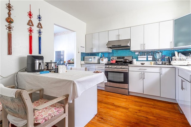 kitchen with tasteful backsplash, stainless steel range with gas cooktop, under cabinet range hood, and white microwave