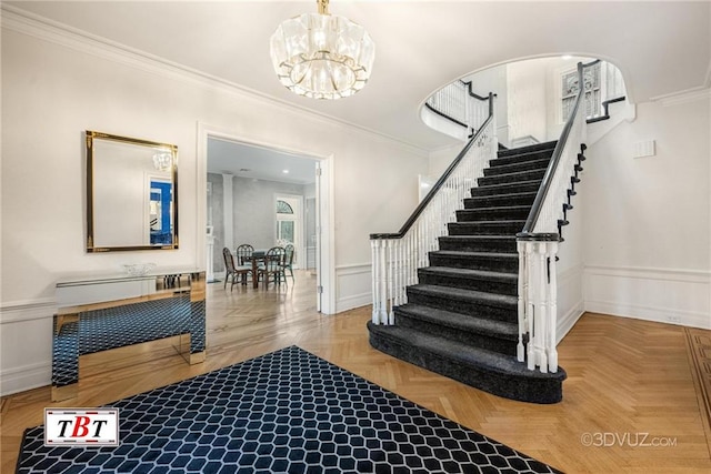 entryway with a chandelier, a decorative wall, a wainscoted wall, ornamental molding, and stairway