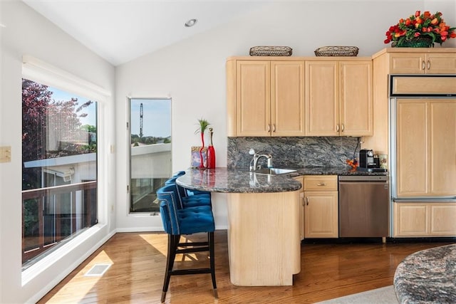 kitchen featuring lofted ceiling, light brown cabinets, stainless steel dishwasher, paneled built in fridge, and dark stone counters