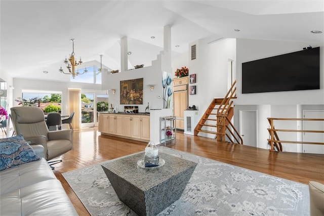 living room with high vaulted ceiling, a chandelier, and light wood-type flooring