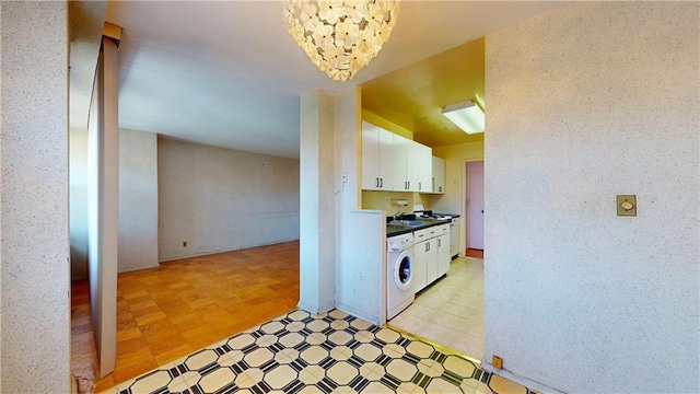 kitchen featuring light floors, dark countertops, an inviting chandelier, white cabinetry, and washer / dryer