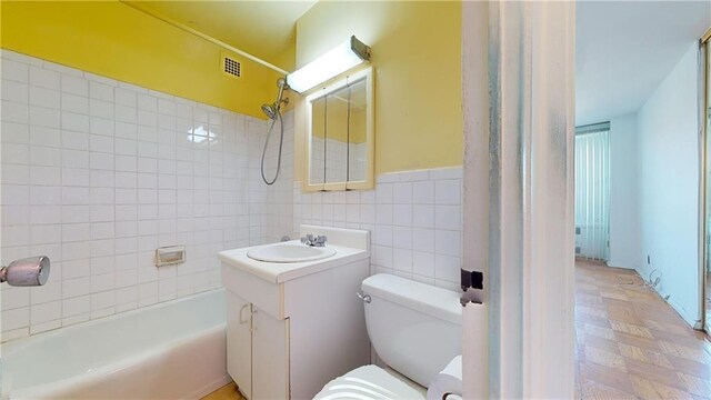 full bathroom featuring tiled shower / bath, vanity, toilet, and tile walls