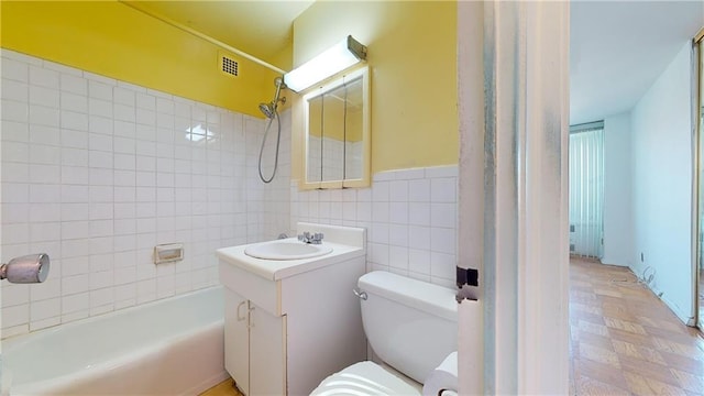 bathroom with visible vents, toilet, tub / shower combination, vanity, and tile walls