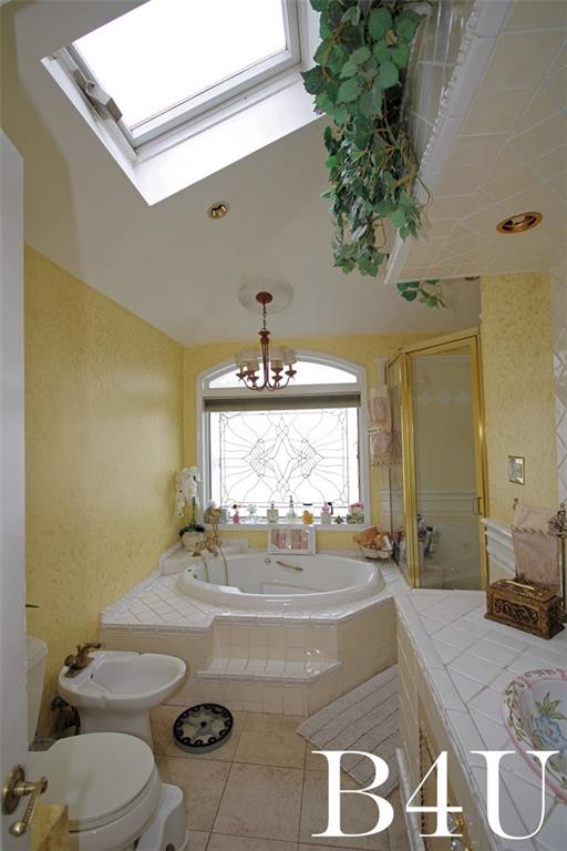 bathroom with a bidet, tile patterned flooring, independent shower and bath, toilet, and vaulted ceiling with skylight