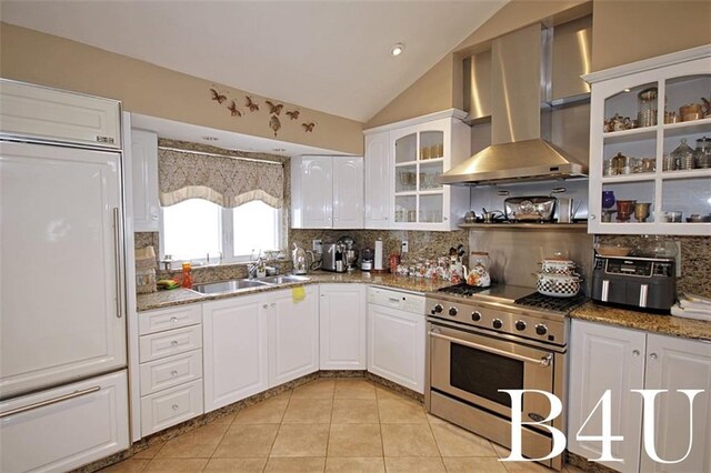 kitchen with wall chimney exhaust hood, high end stainless steel range, vaulted ceiling, white cabinetry, and light tile patterned floors