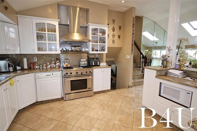 kitchen with dark stone countertops, wall chimney exhaust hood, high end stainless steel range, white cabinetry, and a skylight