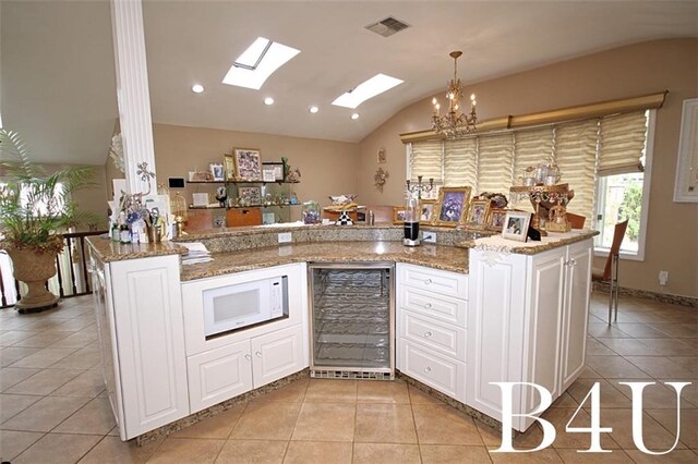 kitchen with vaulted ceiling with skylight, pendant lighting, beverage cooler, light stone countertops, and kitchen peninsula