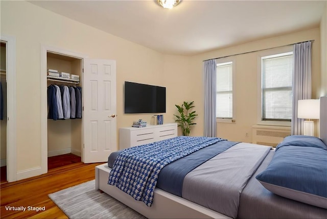 bedroom featuring a walk in closet, wood finished floors, a closet, radiator, and baseboards