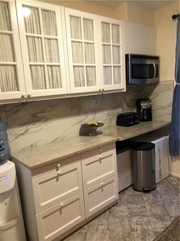 kitchen featuring light stone counters, white cabinets, marble finish floor, backsplash, and stainless steel microwave