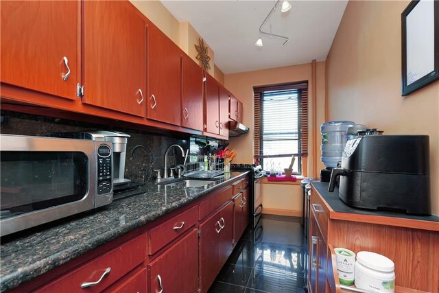 kitchen with tasteful backsplash, rail lighting, sink, dark stone counters, and black range with gas cooktop