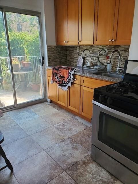 kitchen featuring sink, stone counters, stainless steel gas range oven, and decorative backsplash