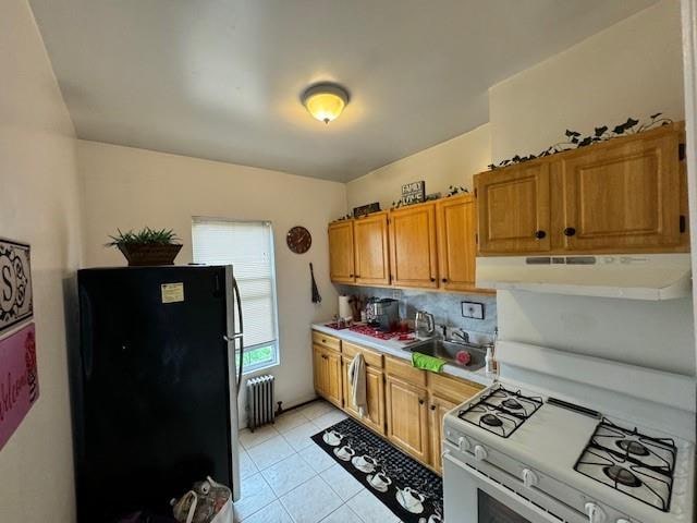 kitchen with light tile patterned floors, sink, white gas stove, radiator heating unit, and stainless steel fridge