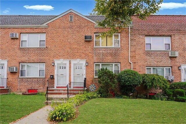 view of front of home with a front lawn and a wall mounted AC