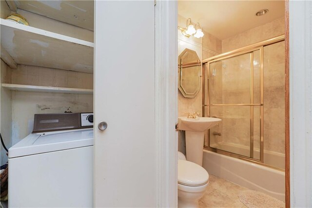 bathroom featuring tile patterned flooring, enclosed tub / shower combo, toilet, and washer / clothes dryer