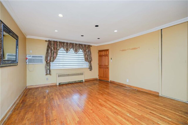 empty room with an AC wall unit, hardwood / wood-style floors, radiator, and ornamental molding