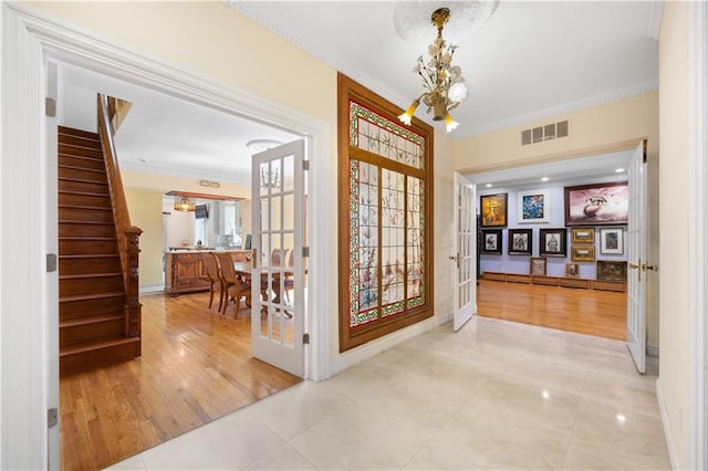 foyer entrance featuring french doors, crown molding, an inviting chandelier, and light tile patterned floors