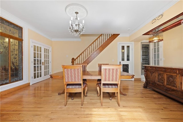 dining area with crown molding, a chandelier, french doors, and light wood-type flooring