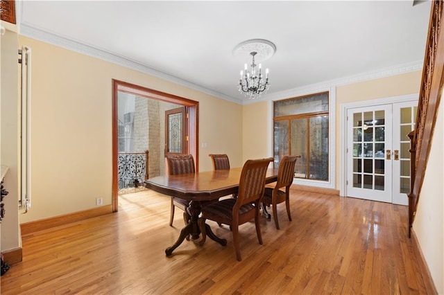 dining space with ornamental molding, a notable chandelier, light wood-type flooring, and french doors