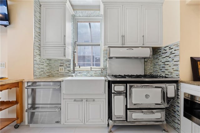 kitchen featuring light tile patterned flooring, sink, white cabinets, backsplash, and stove