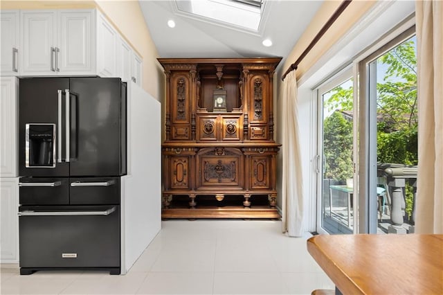 kitchen featuring high quality fridge, lofted ceiling with skylight, light tile patterned floors, and white cabinets