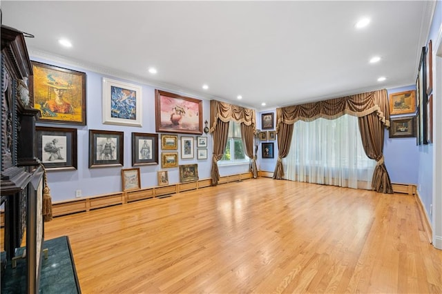 exercise area with a baseboard radiator, ornamental molding, and light wood-type flooring